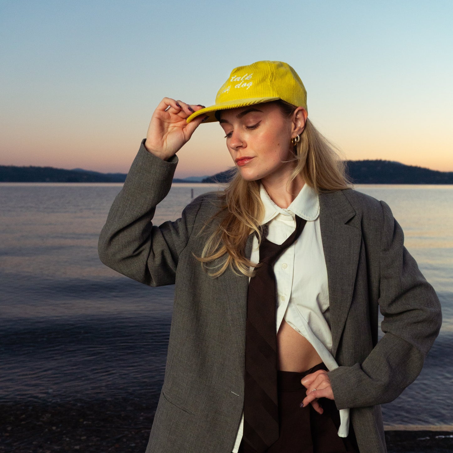 Woman wearing a yellow cap and gray coat by a body of water at sunset