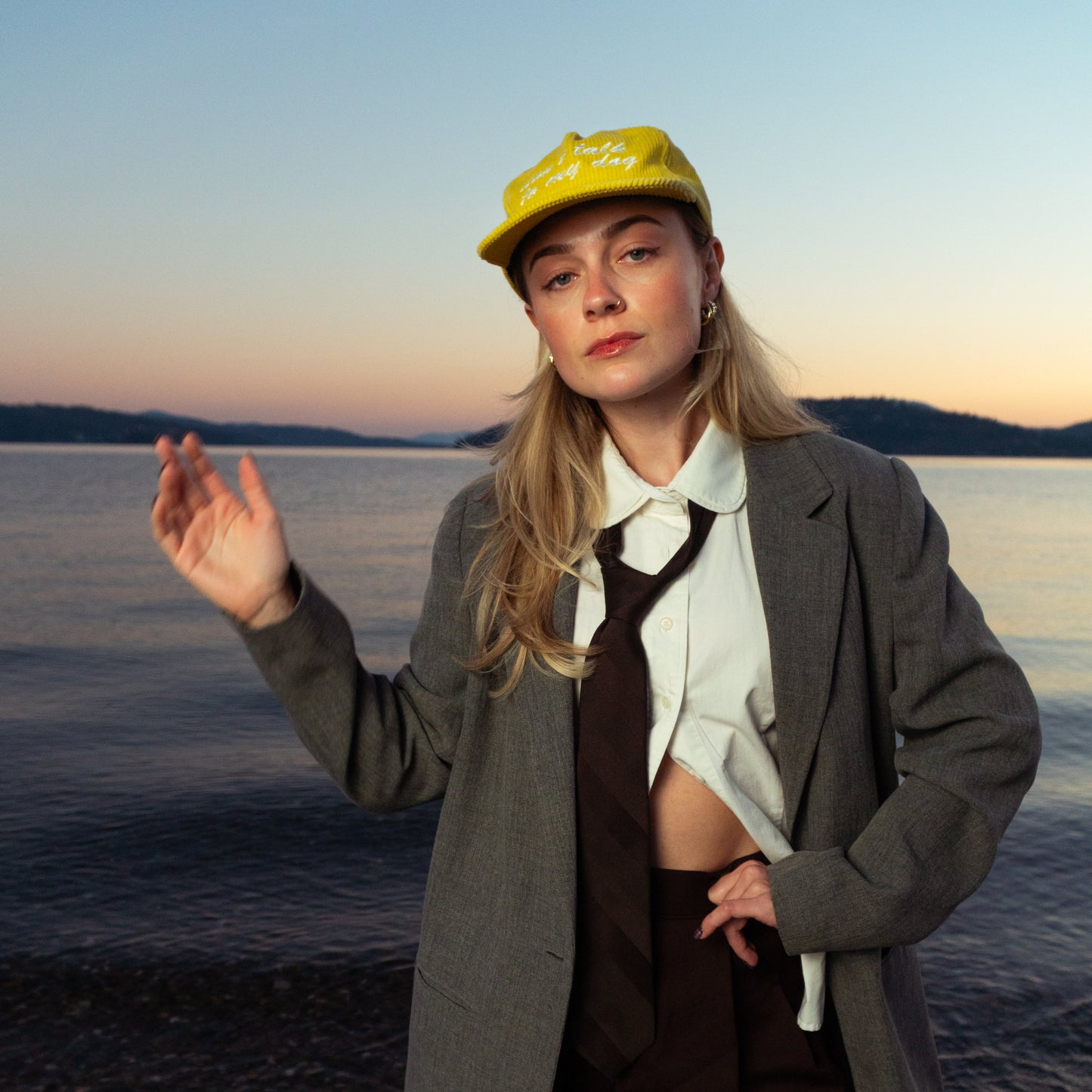 Person wearing a yellow cap and gray coat standing by a body of water at sunset.