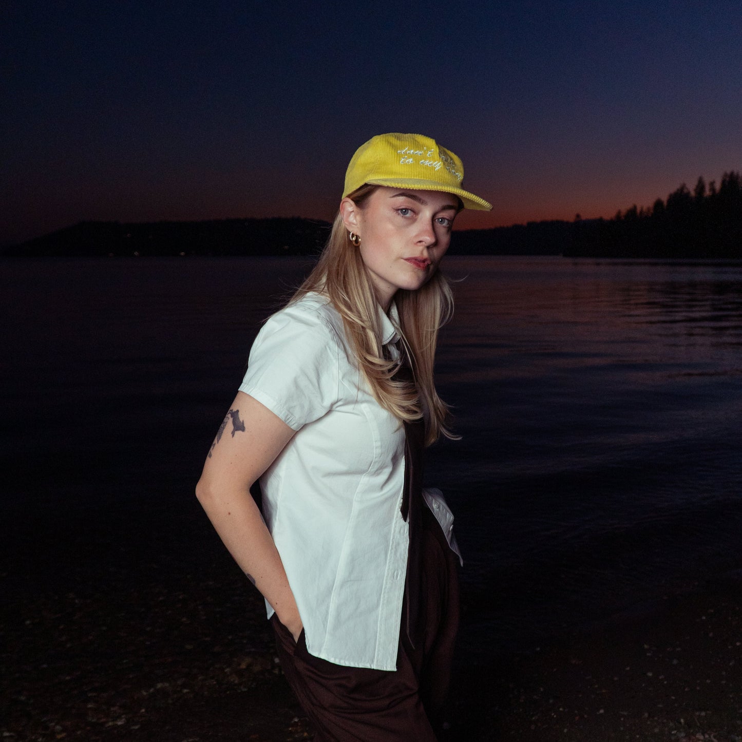 Person wearing a yellow cap and white shirt by a body of water at dusk