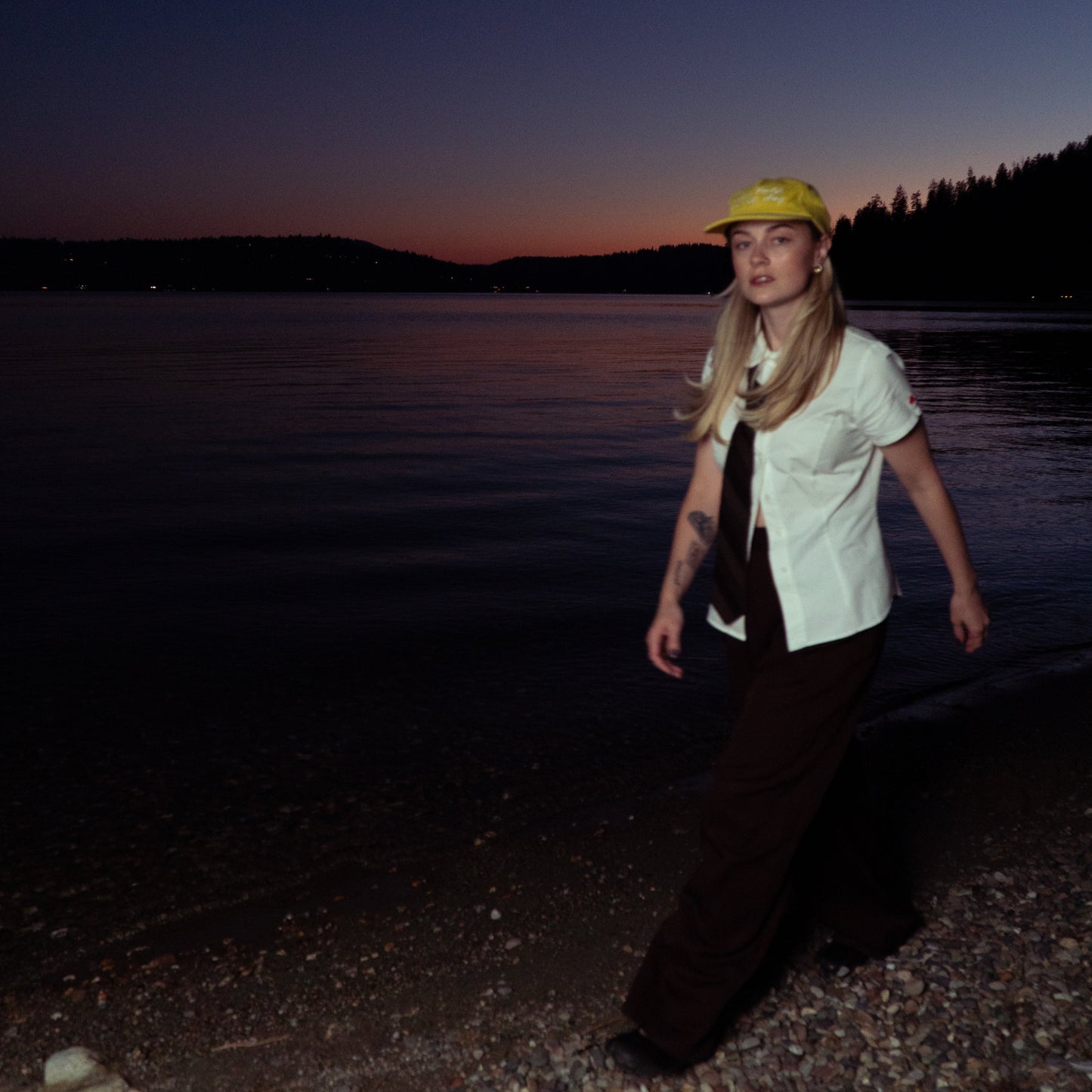 Person standing by a lake at dusk with a dark sky.