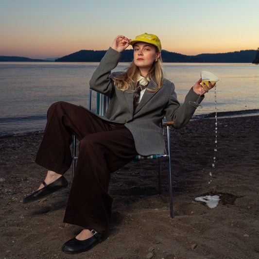 Person sitting on a beach at sunset, holding a drink.