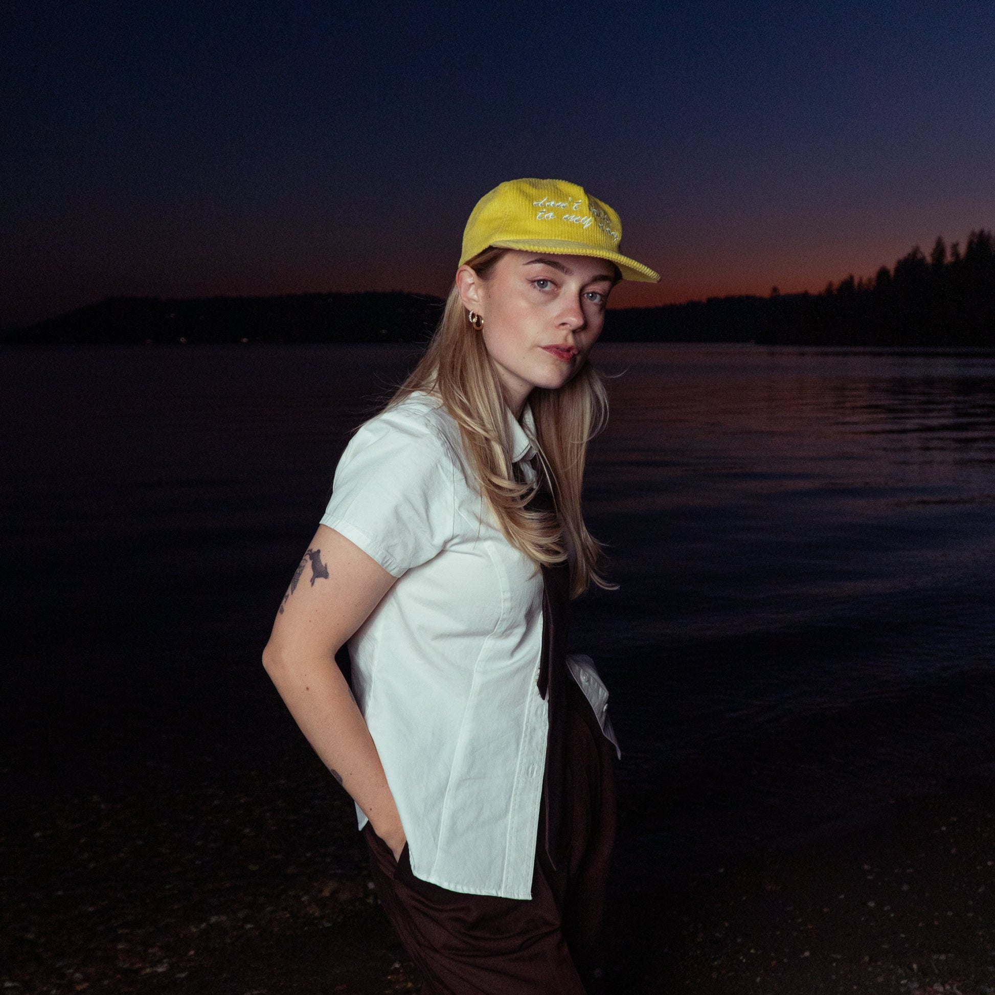 Person wearing a yellow cap and white shirt by a body of water at dusk